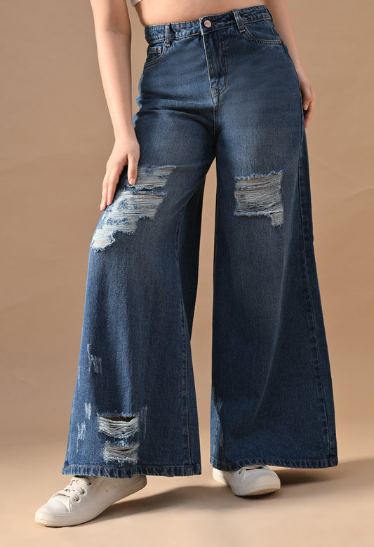 Person wearing blue wide-leg jeans with distressing on a beige background