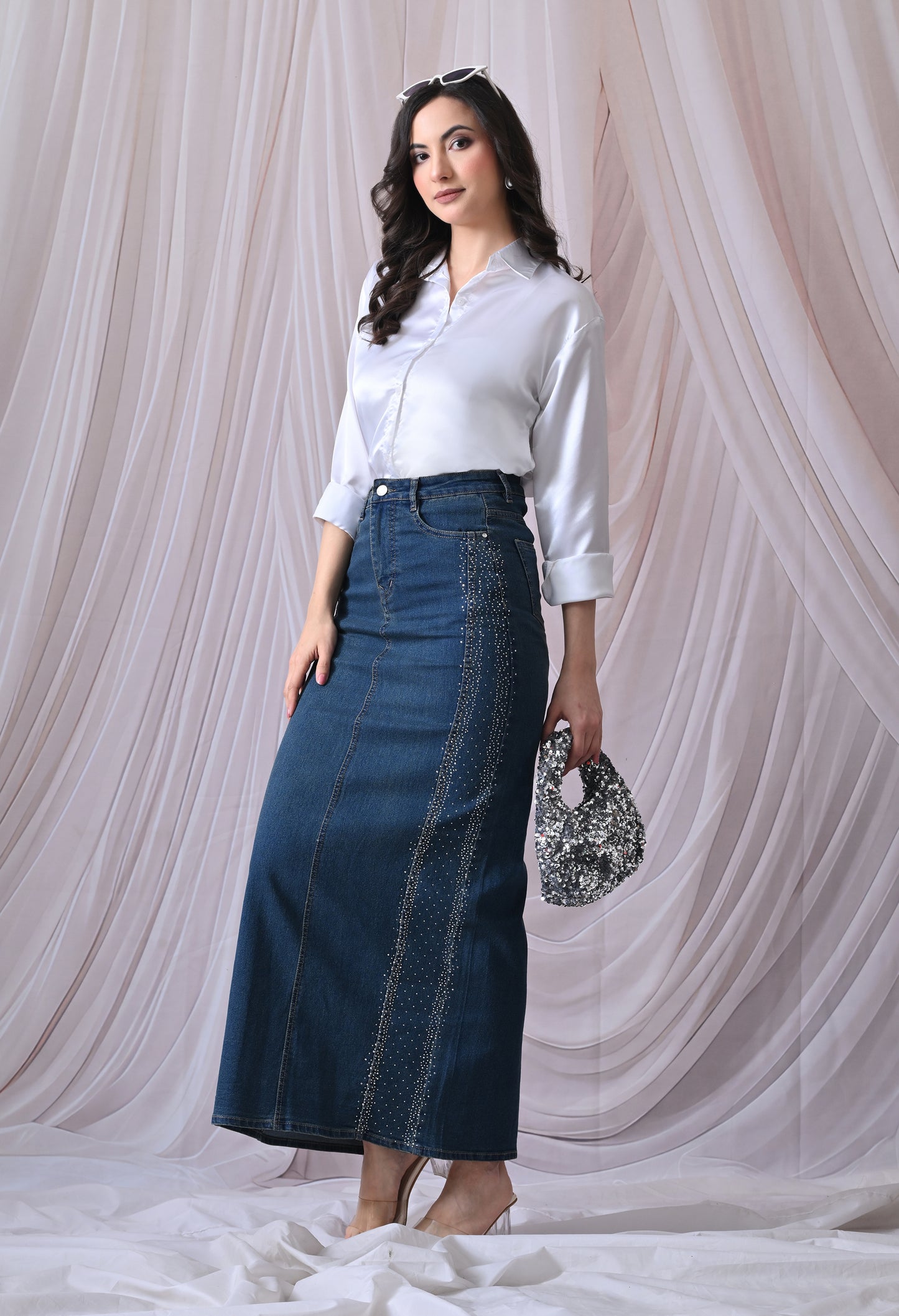 Woman wearing a white blouse and blue denim skirt against a white curtain background