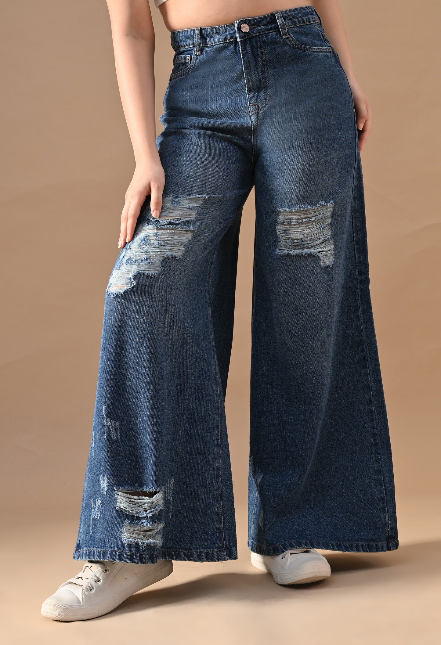 Person wearing blue wide-leg jeans with distressing on a beige background