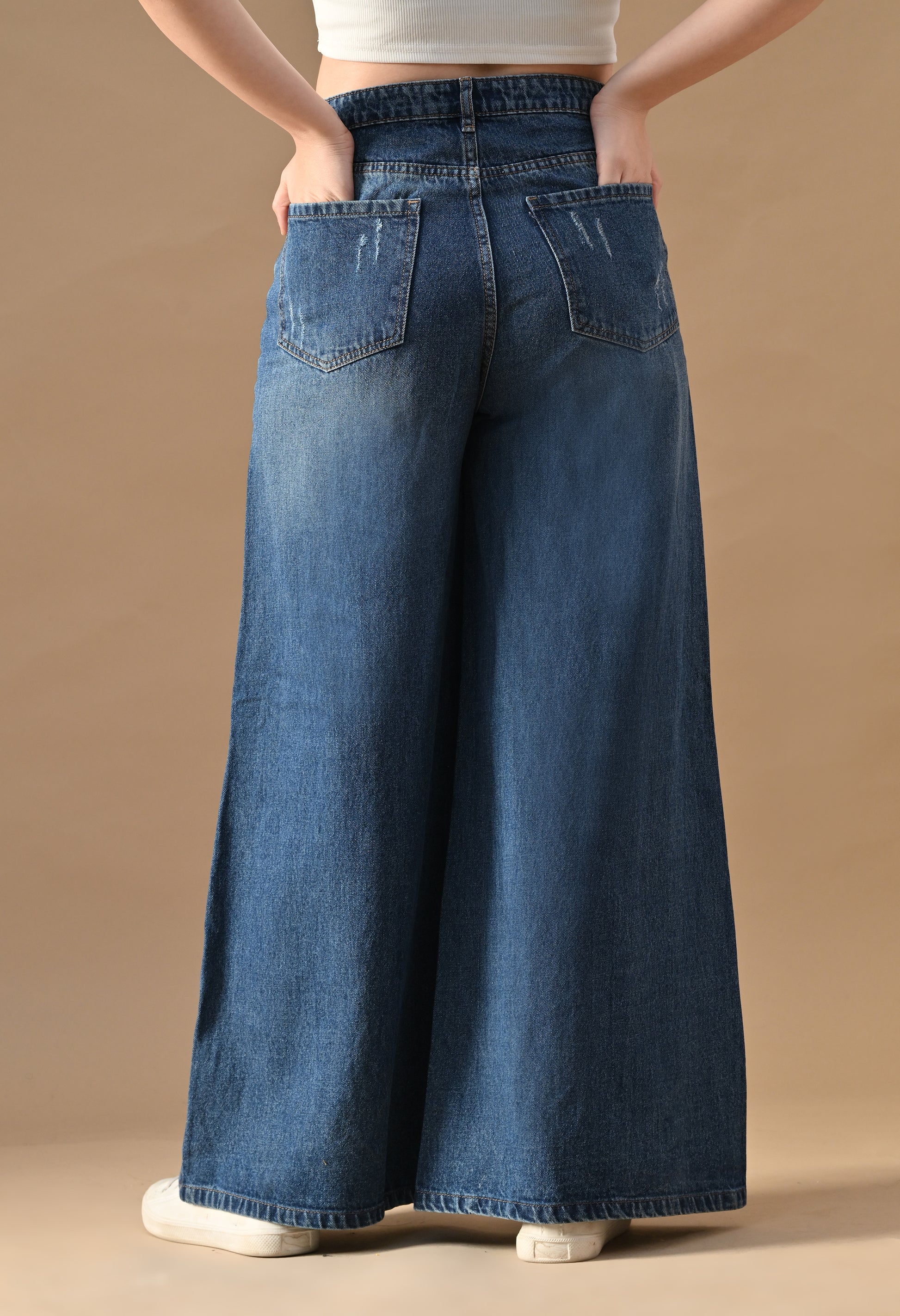 Person wearing blue wide-leg jeans on a beige background